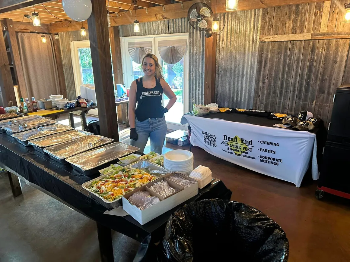 A server standing behind a catering spread of BBQ and sides.